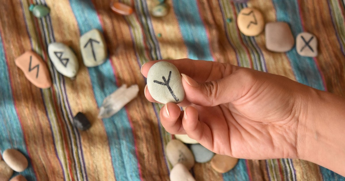 A hand holds a rune stone with runes scattered on colorful striped fabric.