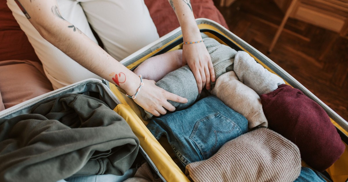 Close-up of a person packing various clothing items into a suitcase, ready for travel.