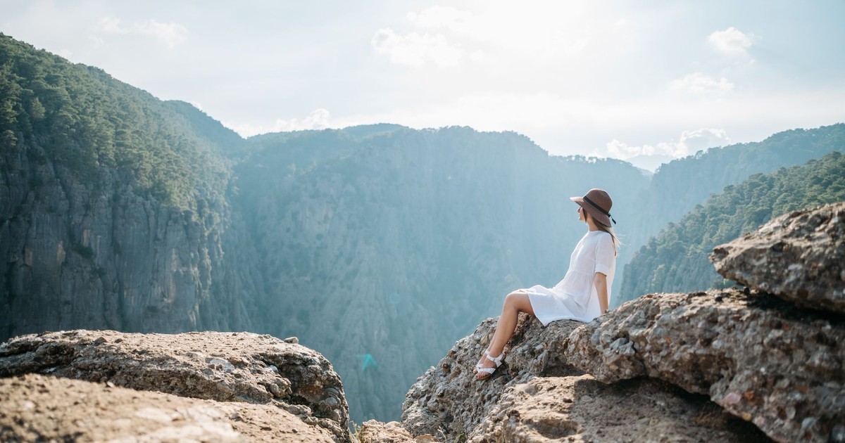 A woman in a white dress sitting on rocks, overlooking a breathtaking mountain view.