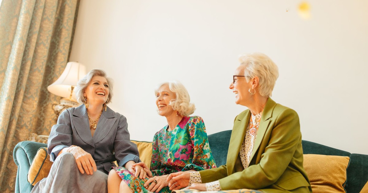 Three senior women laughing together on a couch, exuding elegance and friends