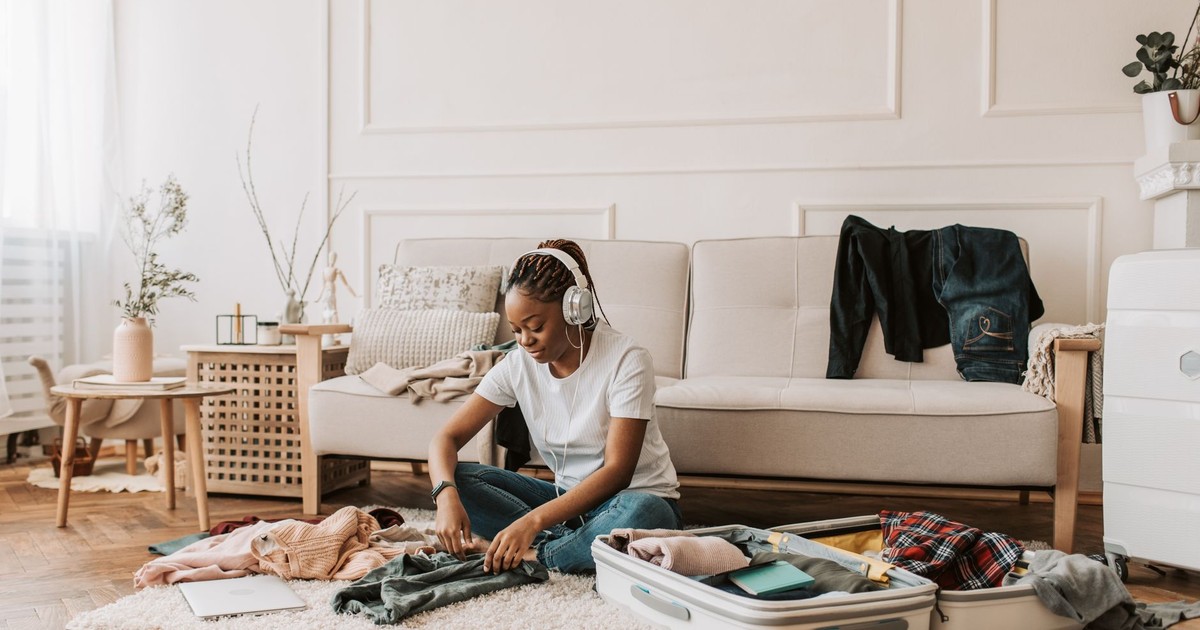 A woman wearing headphones packs a suitcase in a stylish living room, preparing for travel.