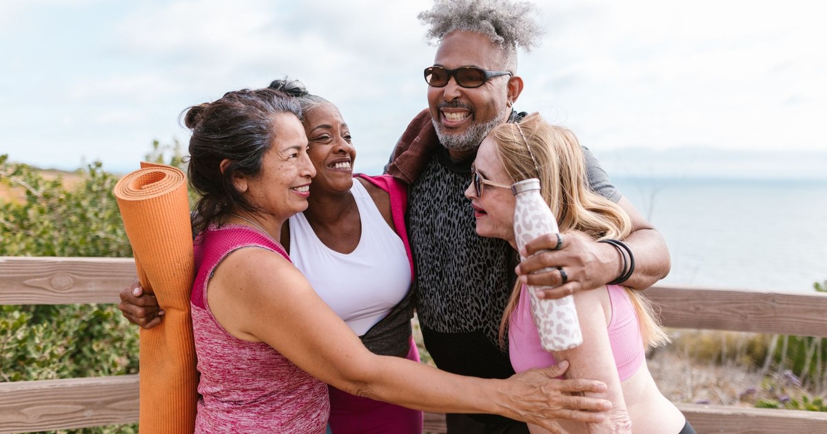 Happy senior friends embracing after a yoga session by the beach, enjoying the outdoors together.