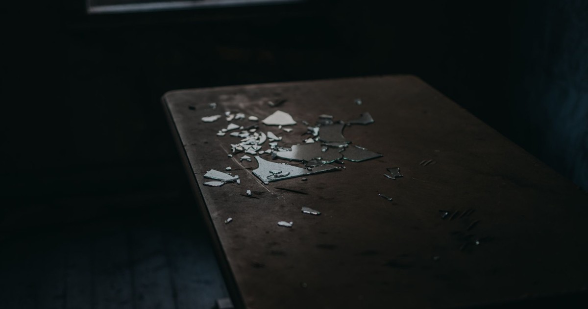 A moody shot of broken glass pieces scattered on an old wooden table in a dimly lit room.