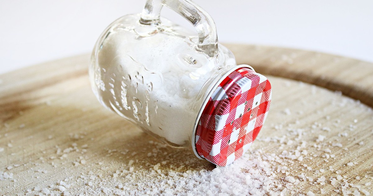 Overturned mason jar with red lid spilling salt on a wooden surface, creating a rustic kitchen scene.