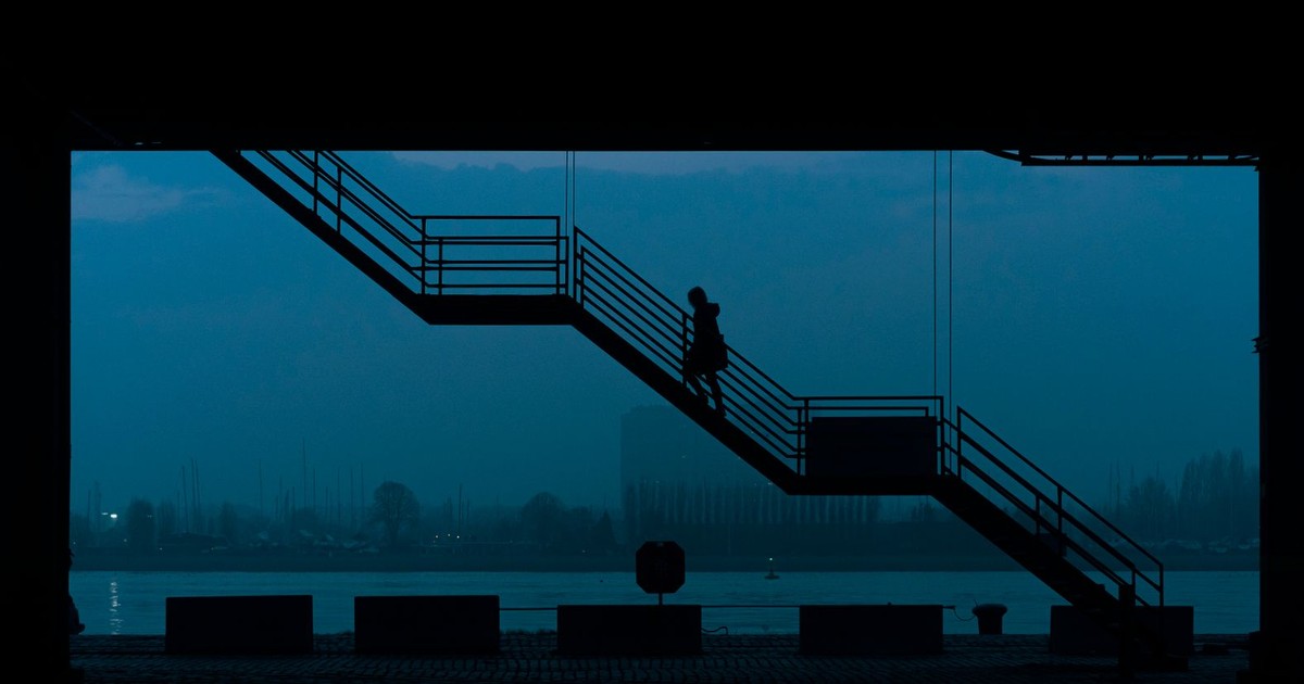 Silhouetted woman walking up stairs in an urban setting during dawn over a river.