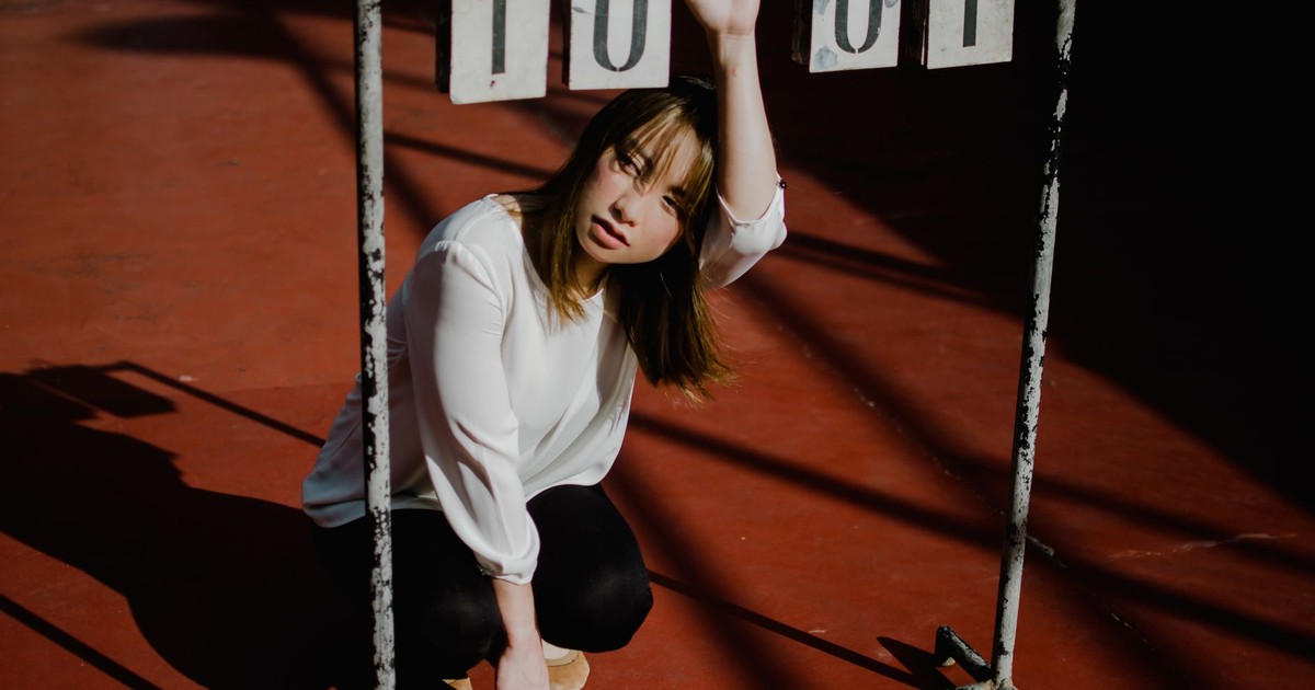 Artistic portrait of a stylish young woman sitting on a red floor with white long sleeves.