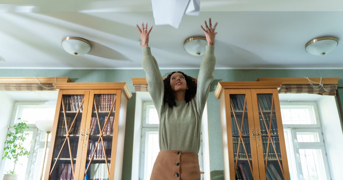 A young woman throws papers in the air in a library, expressing joy and relief.