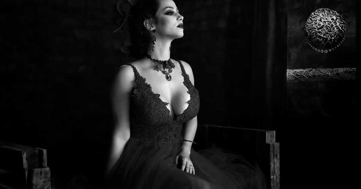 Black and white photo of an elegant woman sitting and posing, showcasing fashion and style.