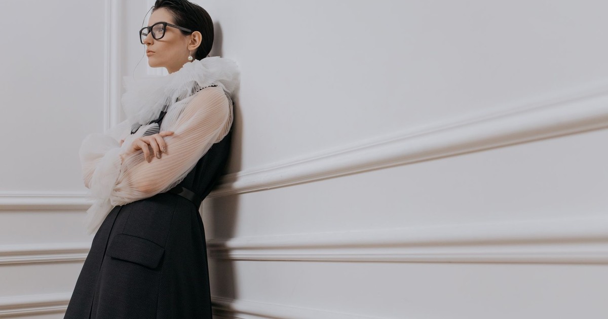 Stylish businesswoman in chic attire standing elegantly against a white wall.