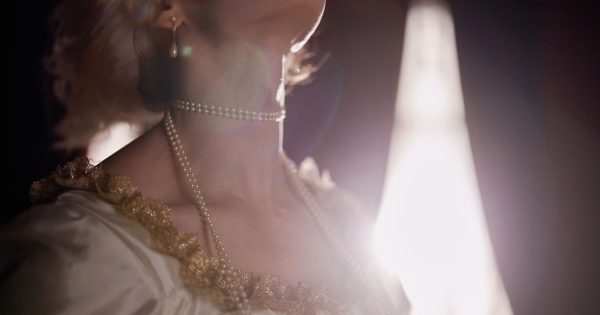 Close-up of a woman wearing a pearl necklace, her head tilted back, illuminated by dramatic lighting.
