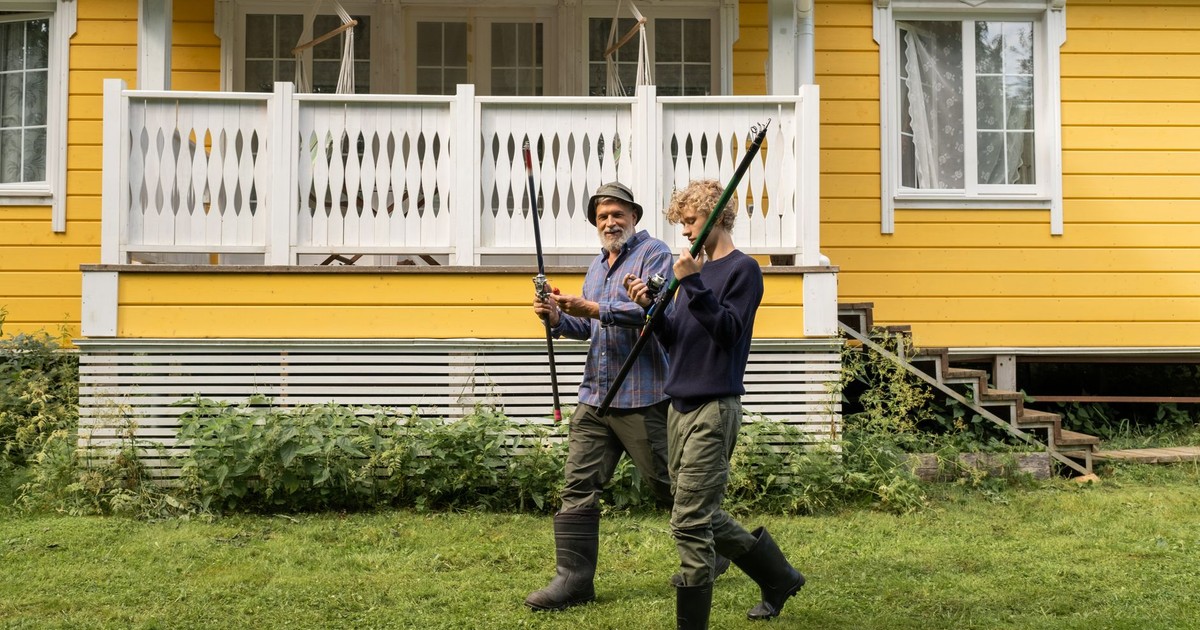 Elderly man and young boy with fishing rods in front of a yellow house, spending quality time outdoors.