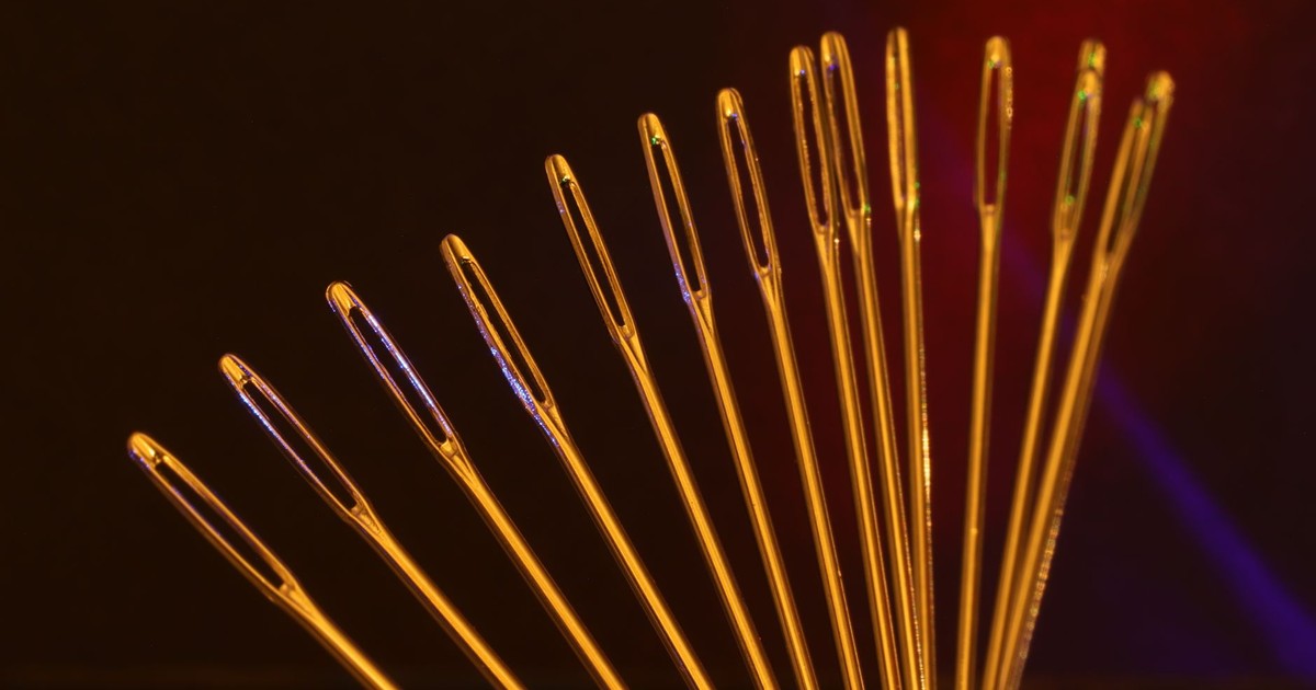 Artistic display of golden sewing needle eyes arranged in an arc against a dark backdrop.