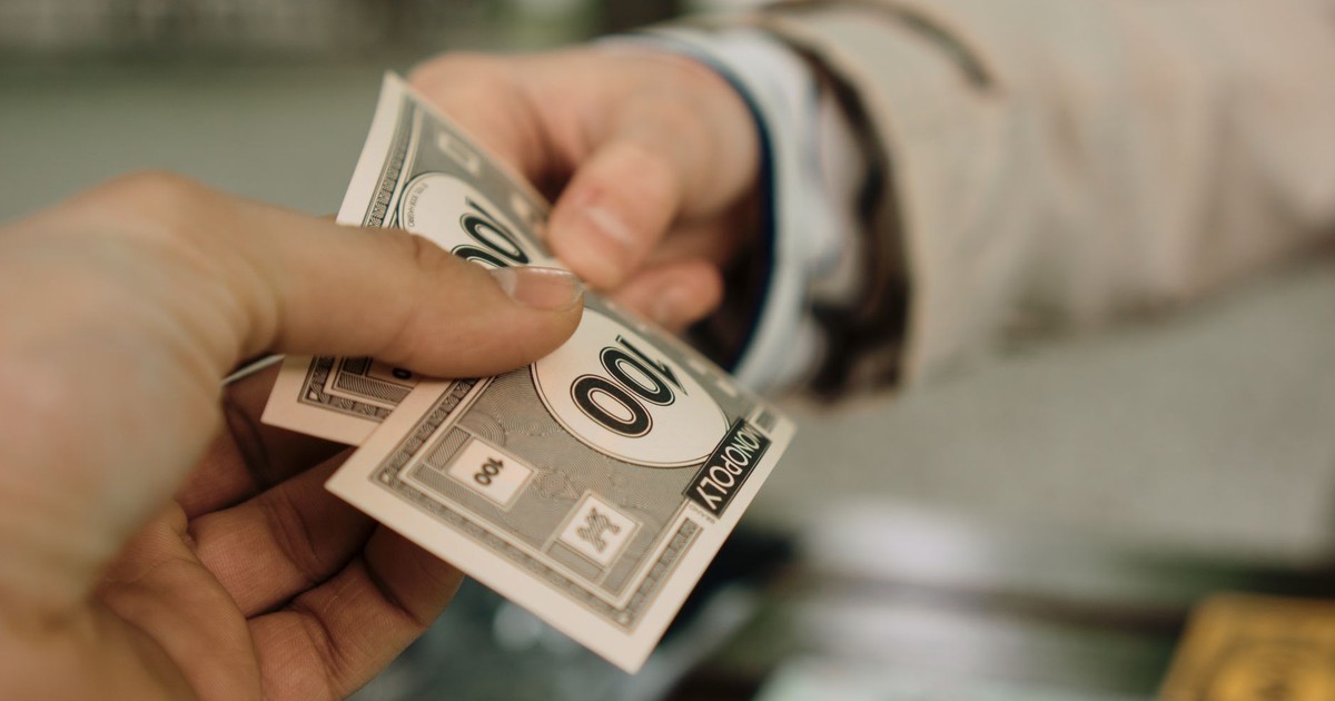 Close-up of two hands exchanging Monopoly money, symbolizing a financial transaction.
