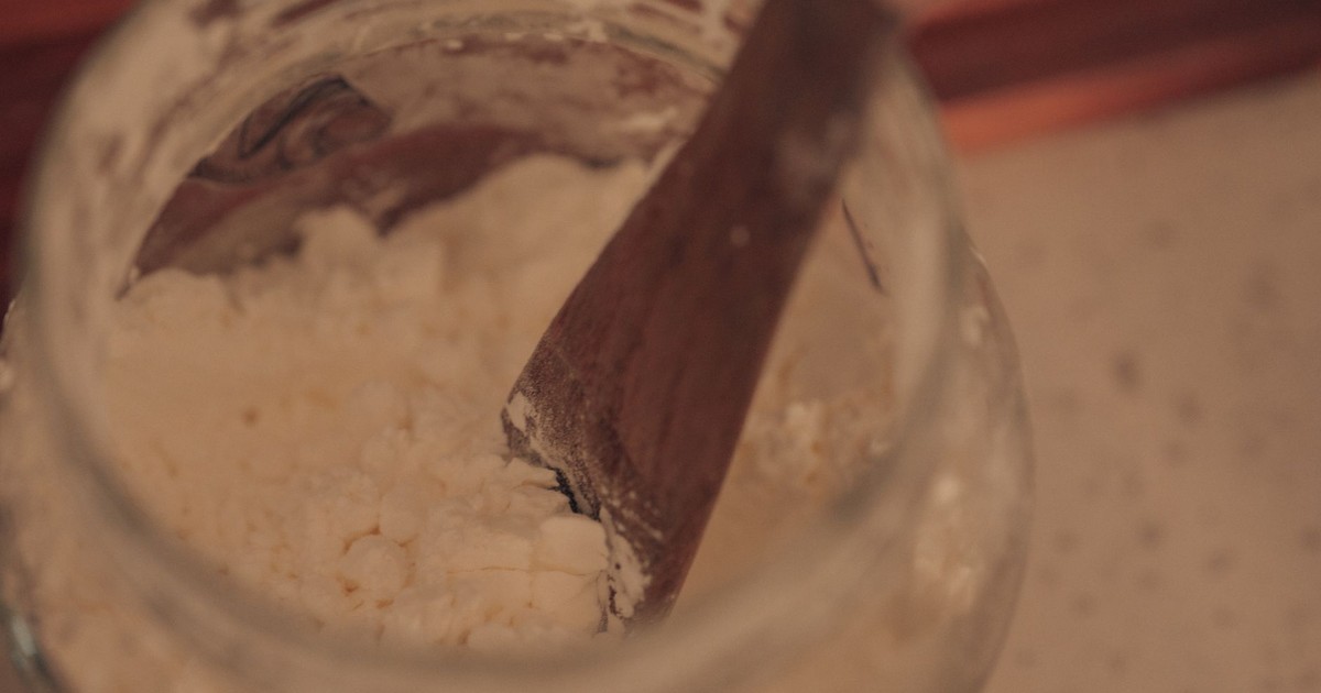 Close-up of wooden spoon stirring powdered ingredient in a glass jar.