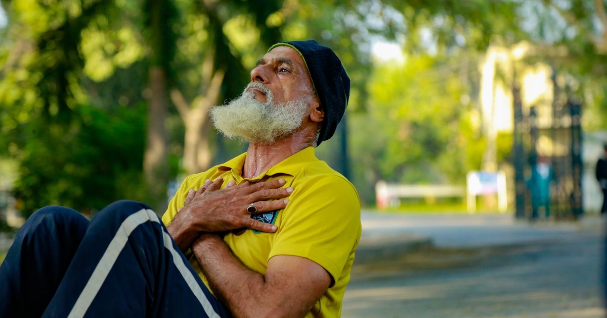 Elderly man performing sit-ups in a sunny park, promoting senior fitness and wellness.