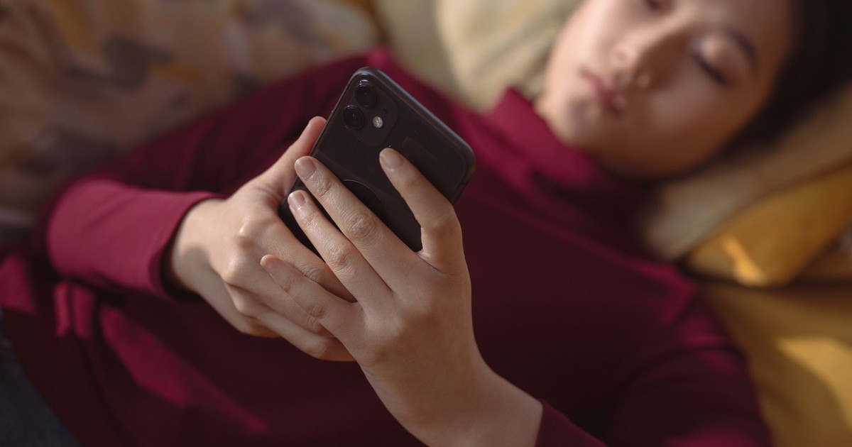 A young woman lying down, holding and using a smartphone for relaxation indoors.