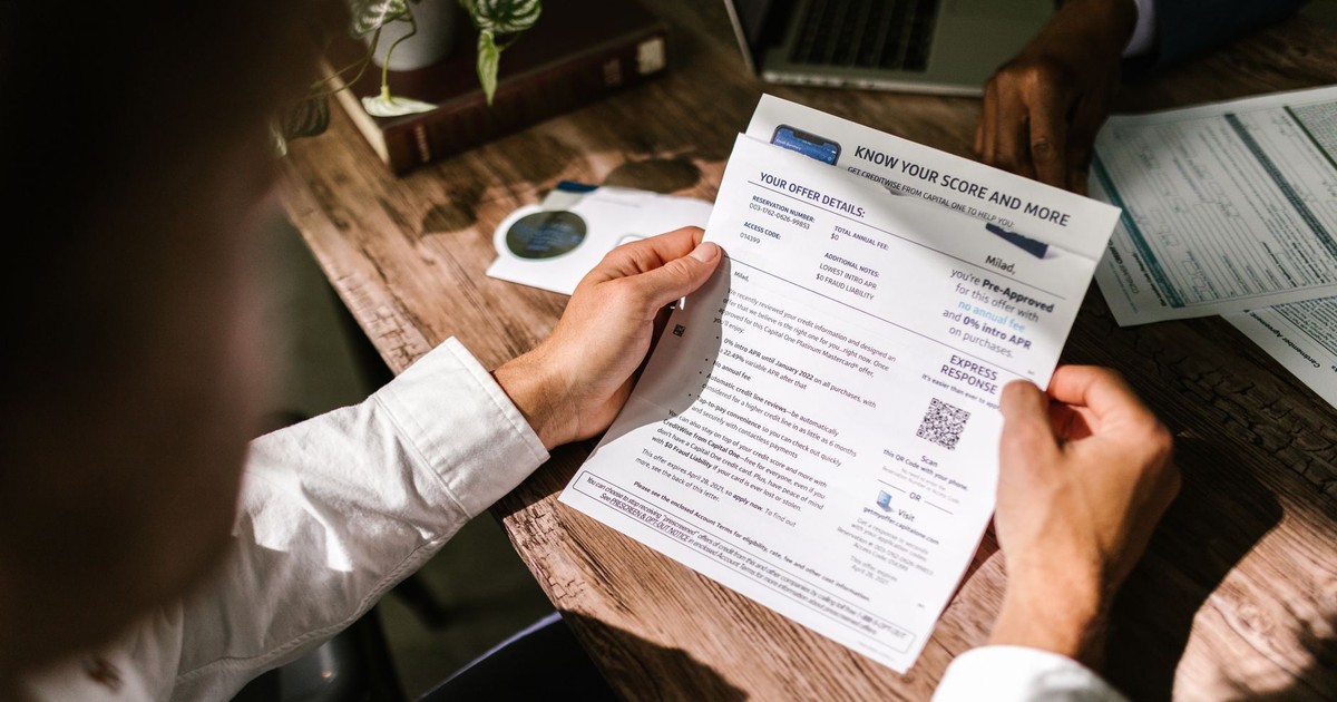 An adult man examining a financial document under natural light at a wooden desk, emphasizing finance and reading.