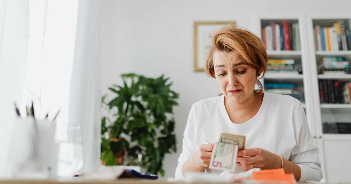 A woman concernedly counts money at her desk in a bright room.