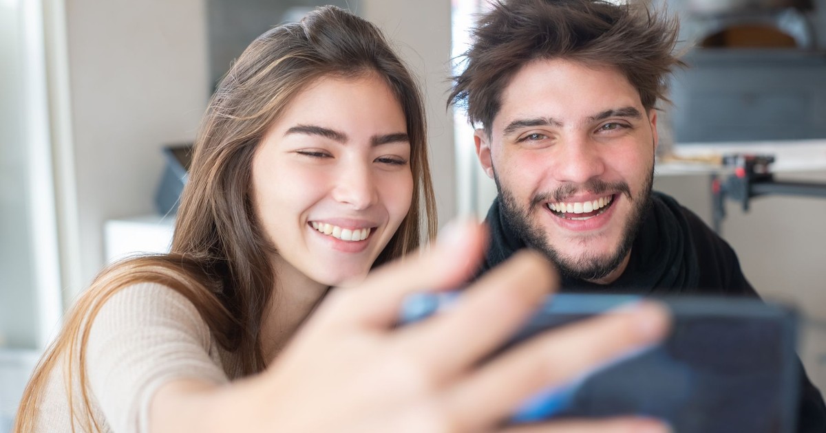Happy young couple taking a selfie indoors, capturing joyful moments together with a smartphone.