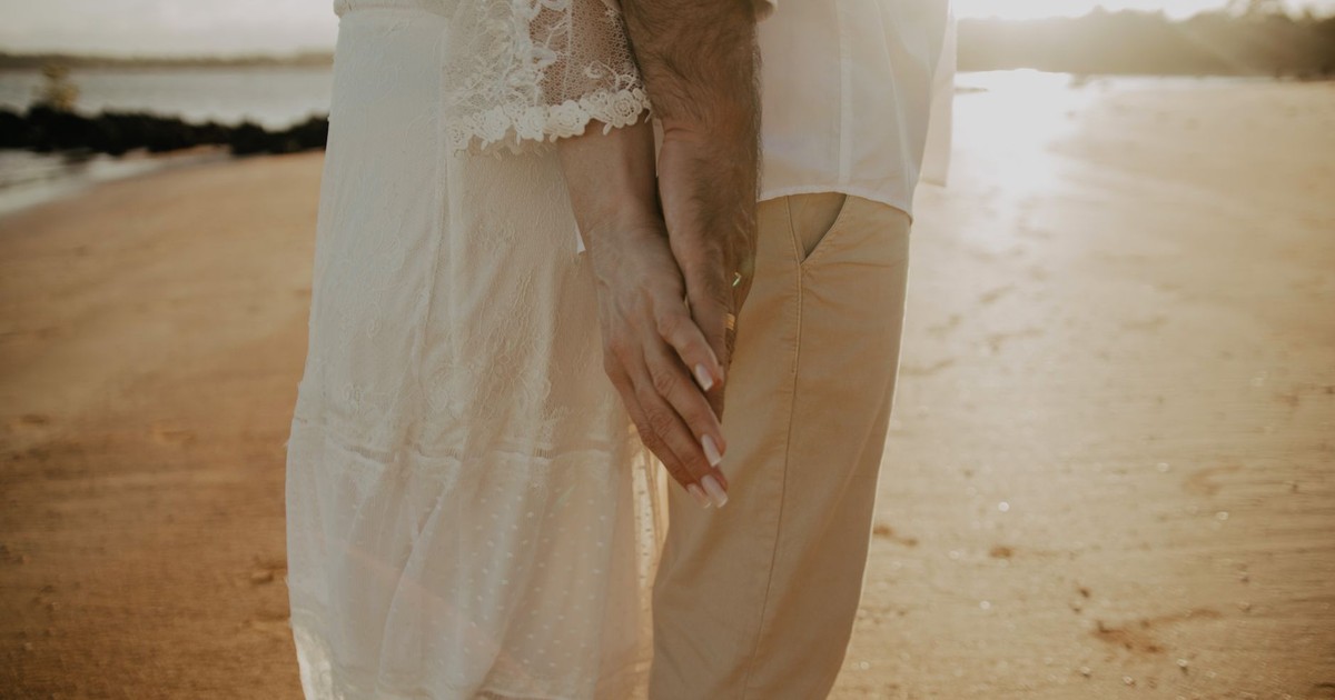 A couple holding hands on a sandy beach during a romantic sunset, symbolizing love and connection.