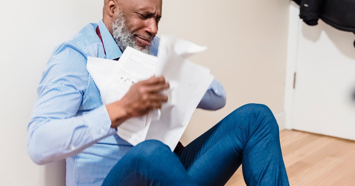 An adult man sitting on the floor, stressed and tearing apart paperwork in frustration.