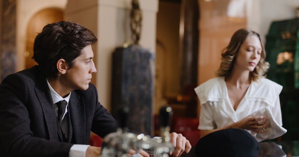 A man and woman engage in conversation at a classic, elegant hotel bar.
