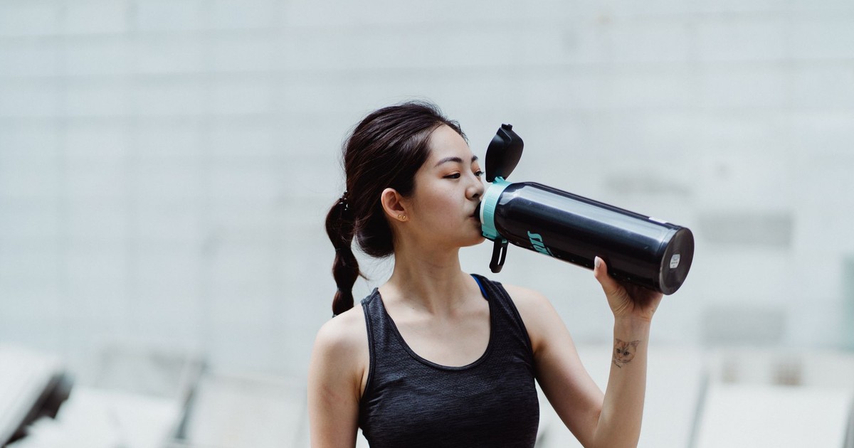 Young woman in workout attire drinks from a water bottle, promoting healthy lifestyle.