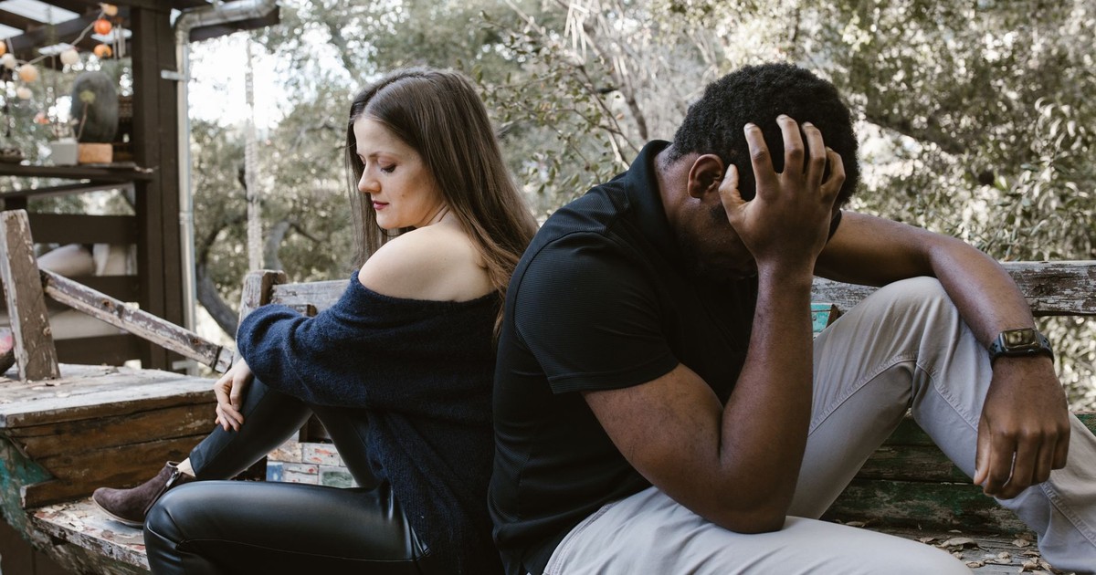 A couple sits back to back on a bench, depicting emotional conflict and loneliness.