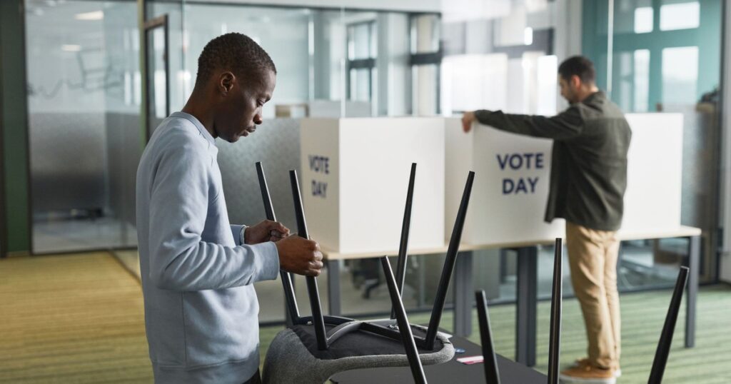 Men preparing voting booths indoors for election day, enhancing democracy.