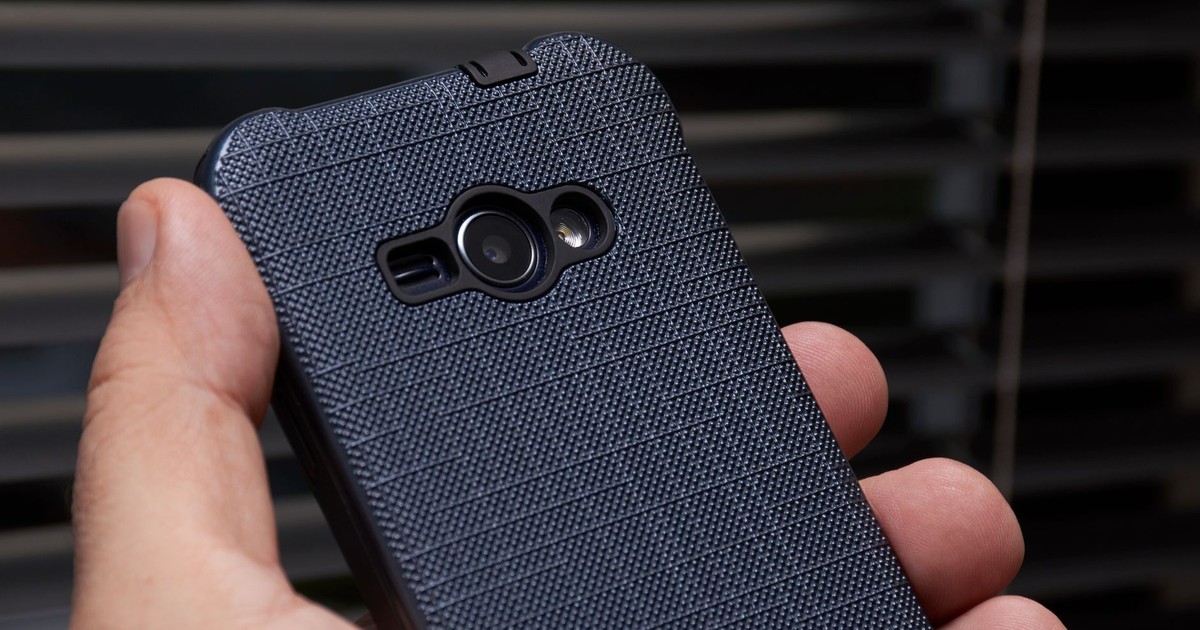 A close-up of a hand holding a smartphone with a textured blue case near a window, showcasing modern technology.