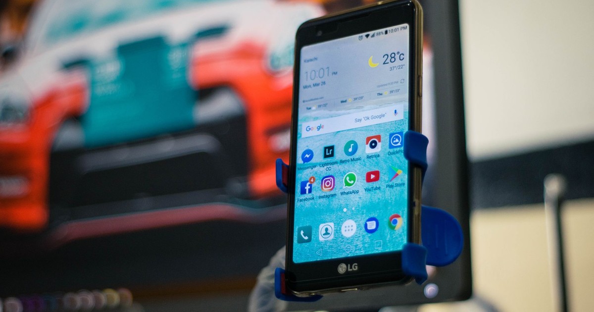 LG smartphone securely mounted in a car holder indoors, displaying various apps on the screen.