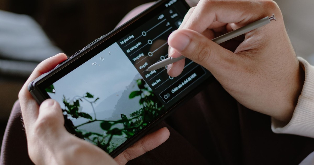 Close-up of a person editing photos on a smartphone with a stylus indoors.