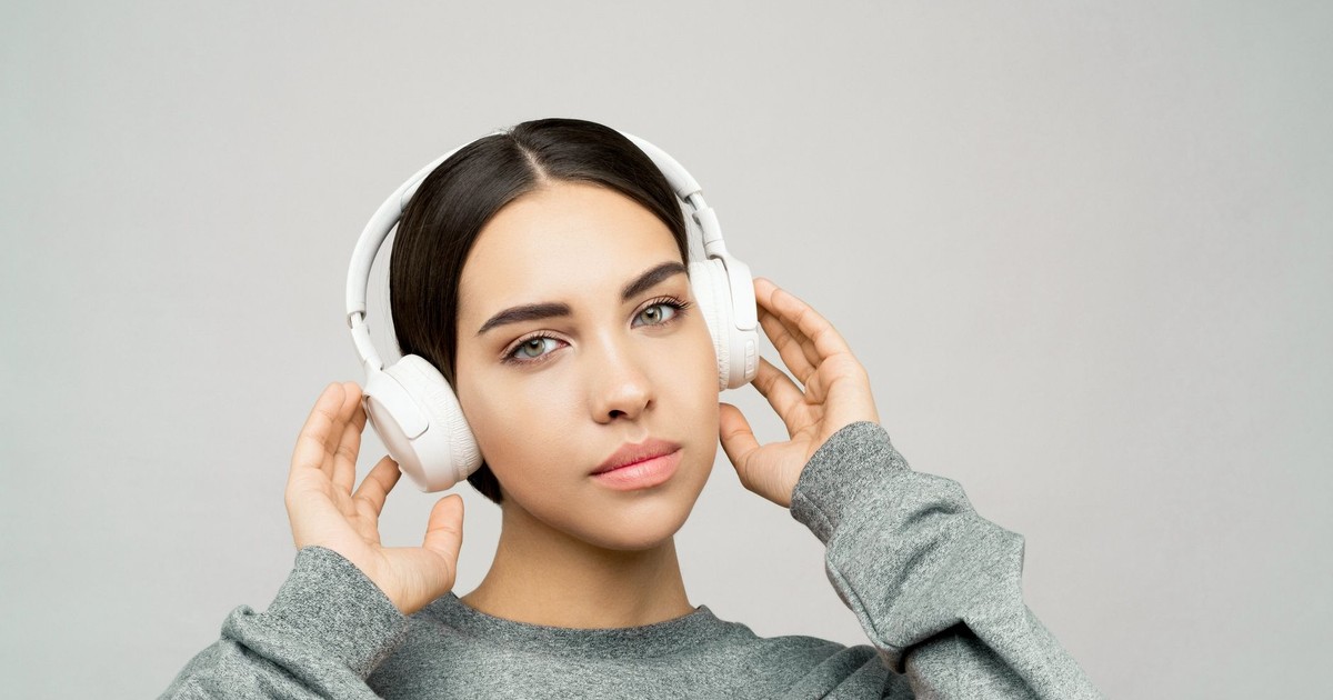 Portrait of a woman in a gray sweater, listening to music with white wireless headphones.