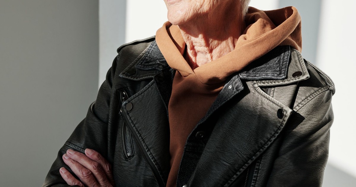 Stylish senior woman in a black leather jacket and brown hoodie smiling indoors.