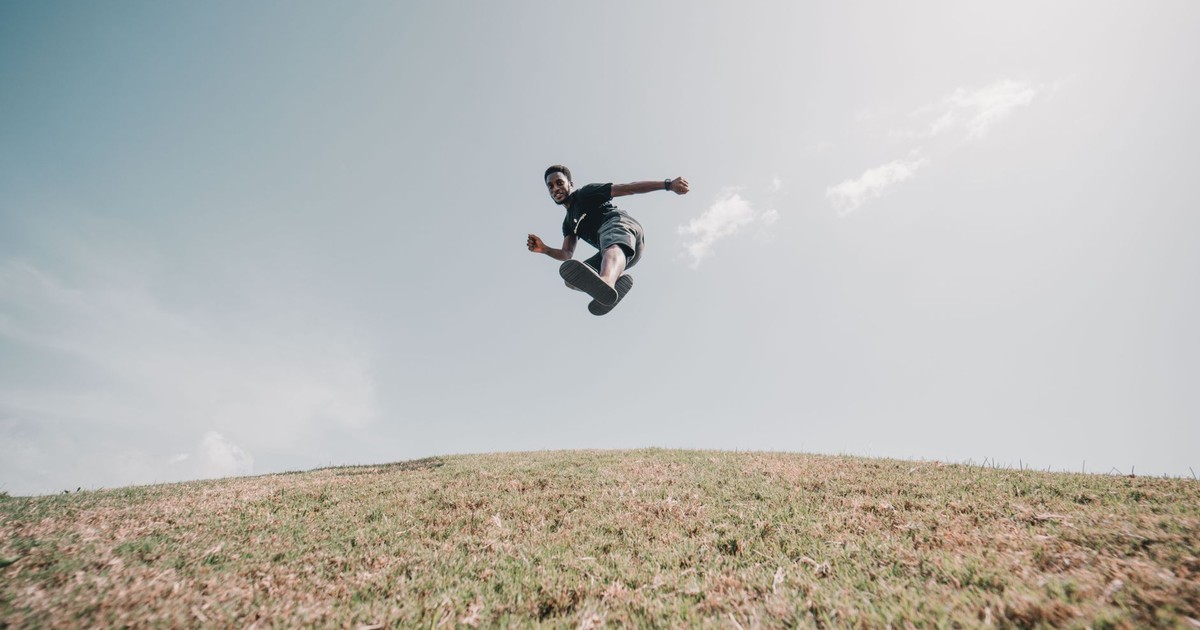 Dynamic shot of a man jumping joyfully on a grassy hill under a clear sky, capturing a moment of freedom.