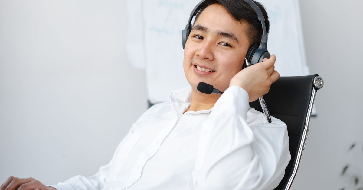 Asian call center agent sitting at desk with headset, smiling.