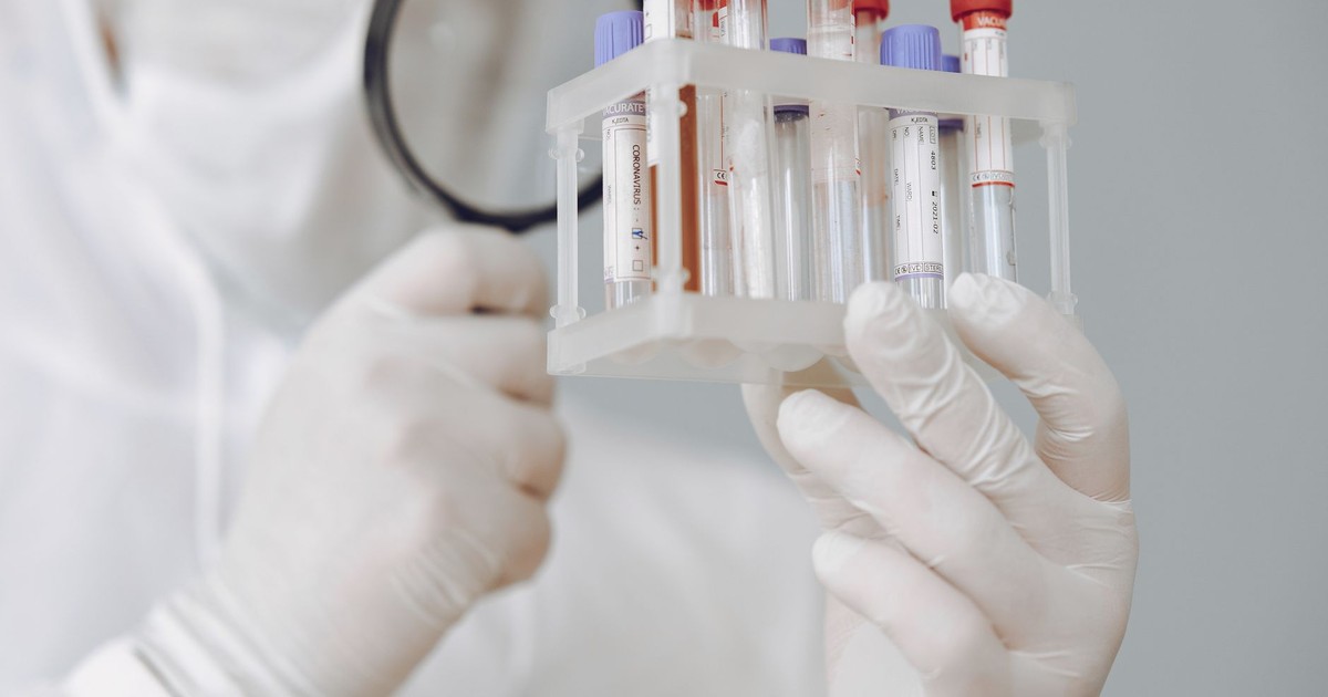 A laboratory scientist examines blood samples using protective gear and a magnifying glass.