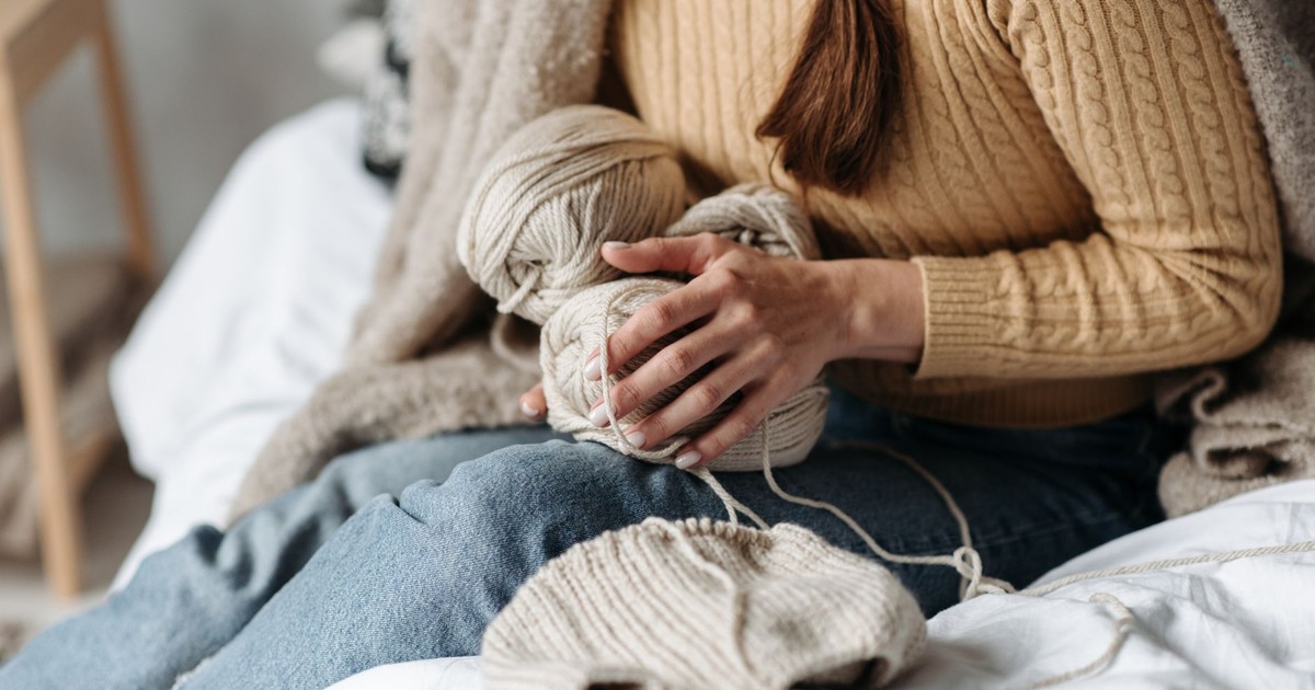 Female knitter crafting with beige yarn on a cozy bed, embodying a warm indoor setting.