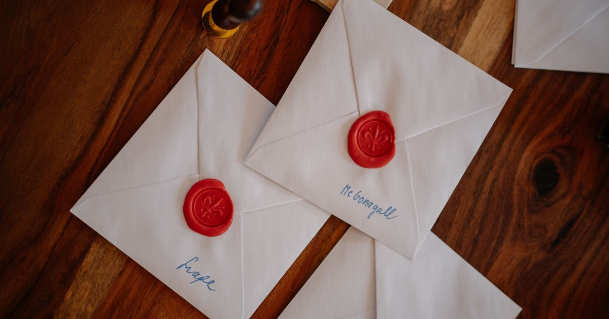 Three white envelopes sealed with red wax are creatively displayed on a wooden table, suggesting a vintage theme.
