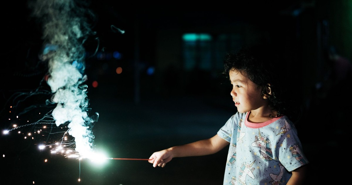 A young child joyfully holding a sparkler at night, creating a magical glowing effect.