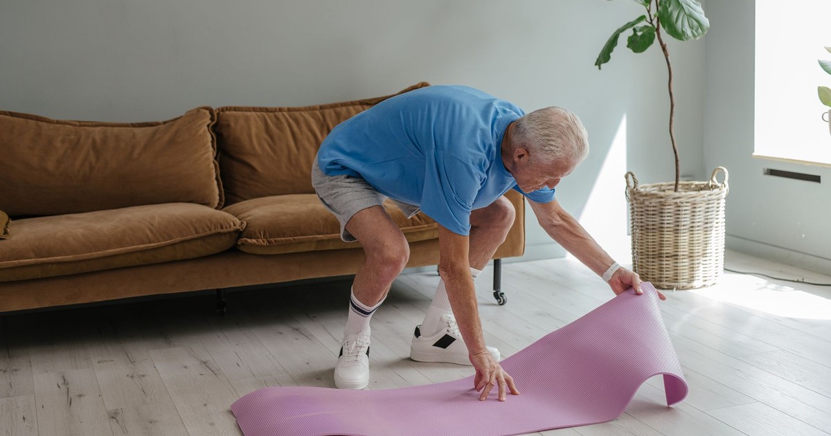 An elderly man sets up his yoga mat indoors, embodying a healthy lifestyle.