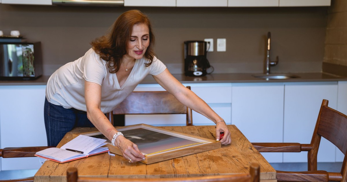 Senior woman arranging a picture frame on a wooden table in a modern kitchen setting.