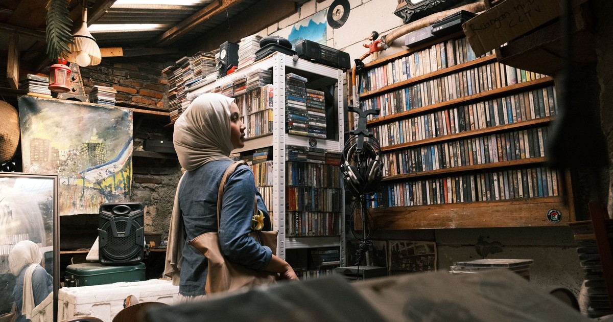 A woman in a hijab explores a vintage music room filled with cassettes in Jakarta, Indonesia.
