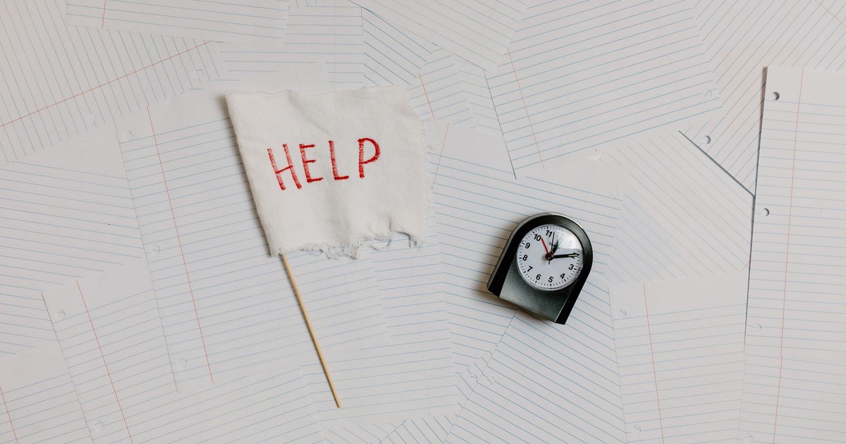 A flat lay image depicting stress and overwork with a help flag and clock on papers.