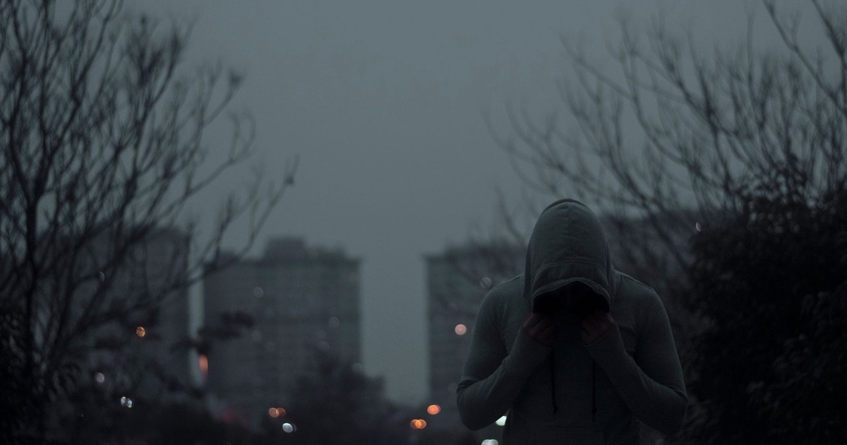 Person in gray hoodie in a dimly lit urban environment with a moody ambiance.
