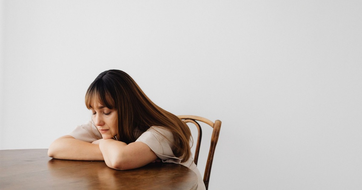 A calm and serene portrait of a woman resting with eyes closed at a wooden table.