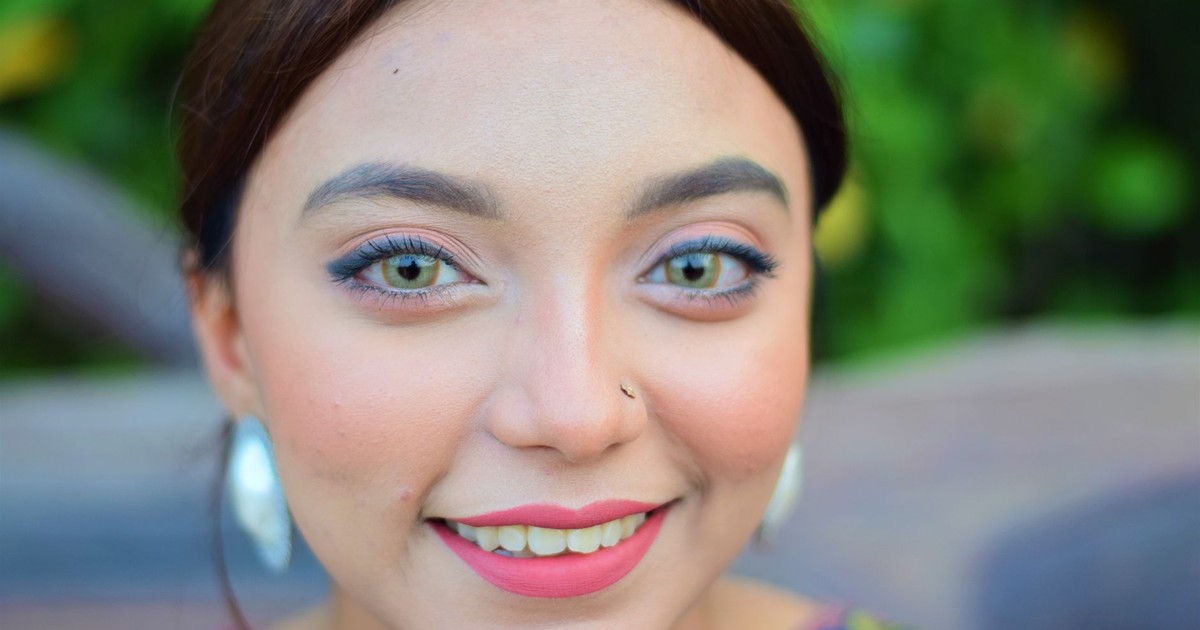 A vibrant portrait of a smiling woman with colorful eyes and nose ring, set against a green background.