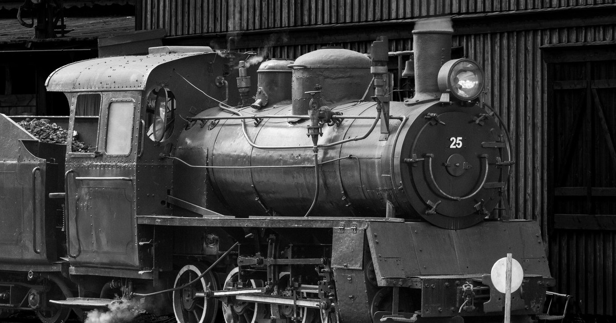 Black and white image of a historic steam train engine at a station.