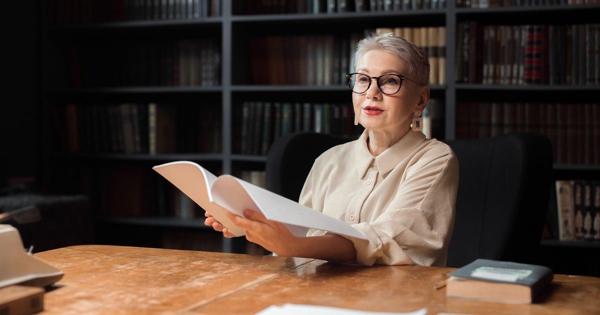 Elderly woman engaging with a book in a cozy library environment.