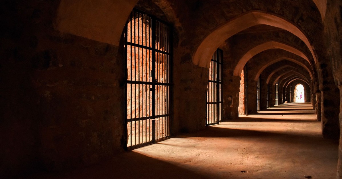 Dramatic lighting in an ancient stone corridor with gothic arches and barred gates.